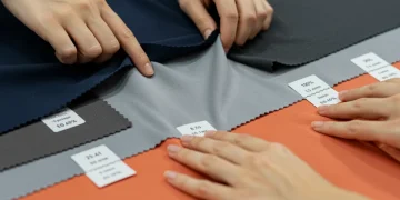 Hands stretching various fabric swatches with different elastane percentages, demonstrating elasticity.